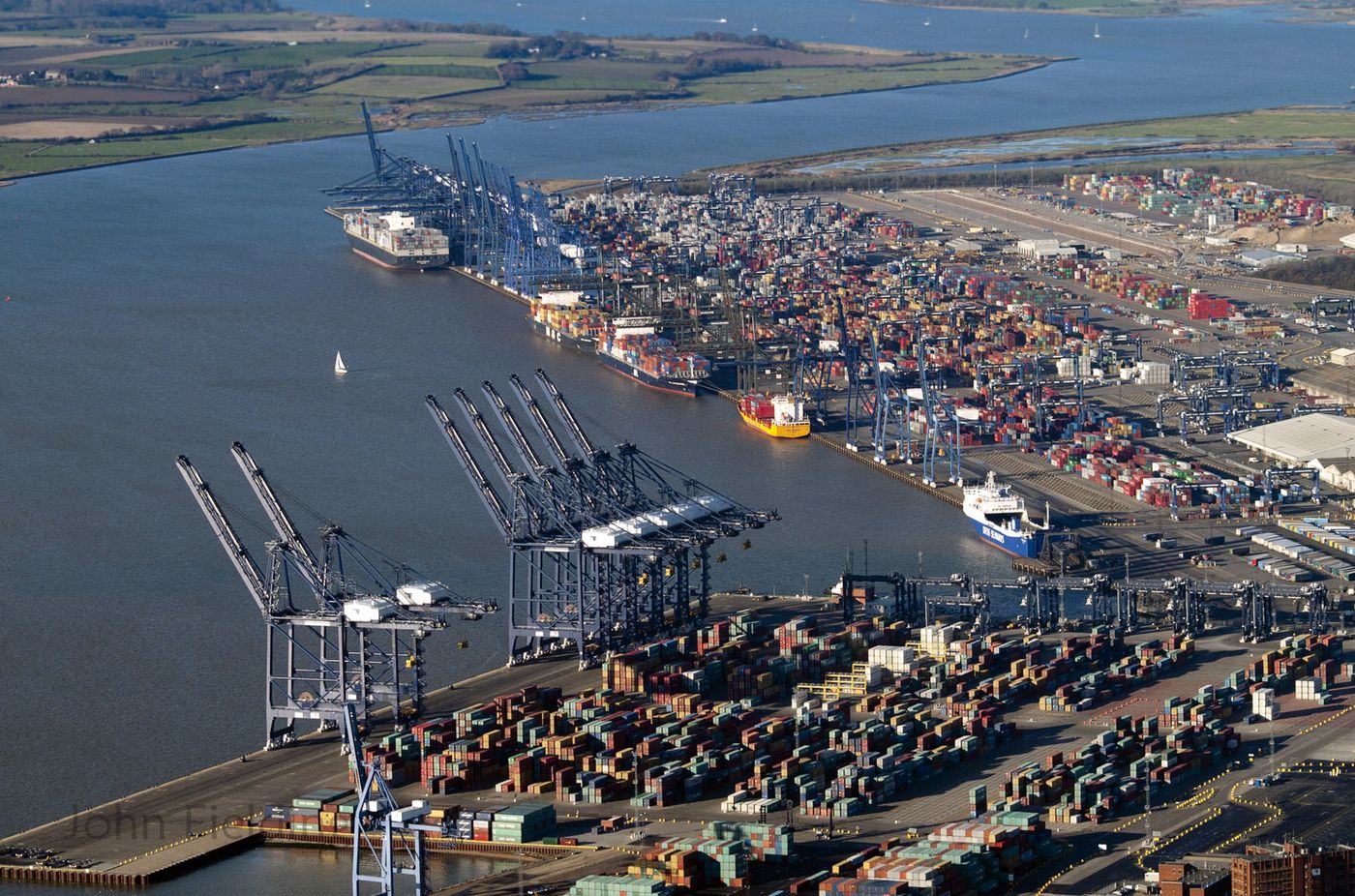 Aerial view of a UK container port with quayside cranes and stacked containers.